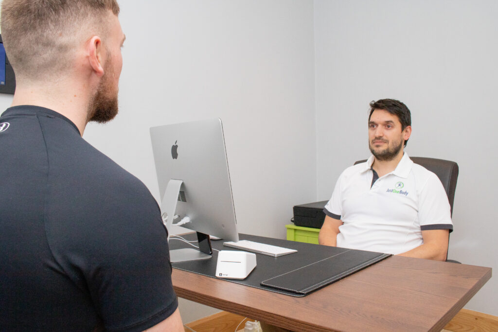 Osteopath listening to a patient at his desk during a consultation at Just One Body, New Ross