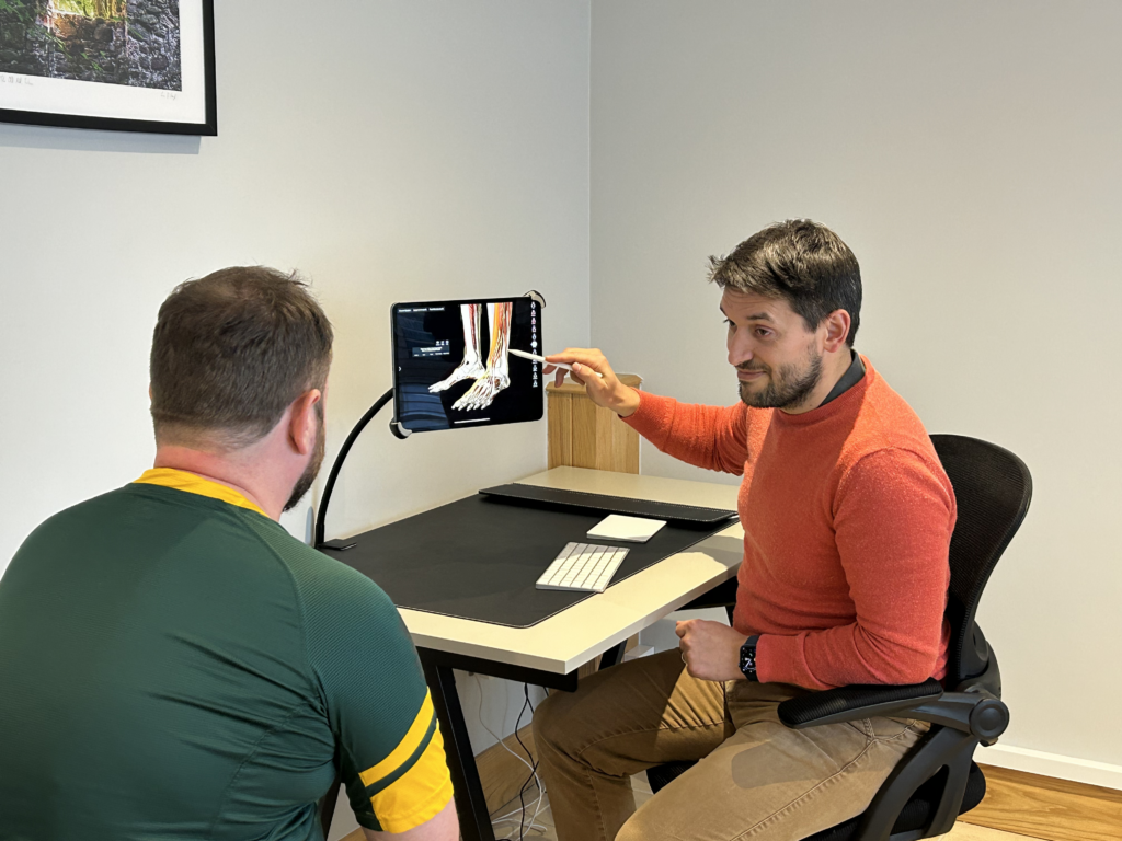 Osteopath explaining an anatomy image on an iPad to a patient at Just One Body, New Ross