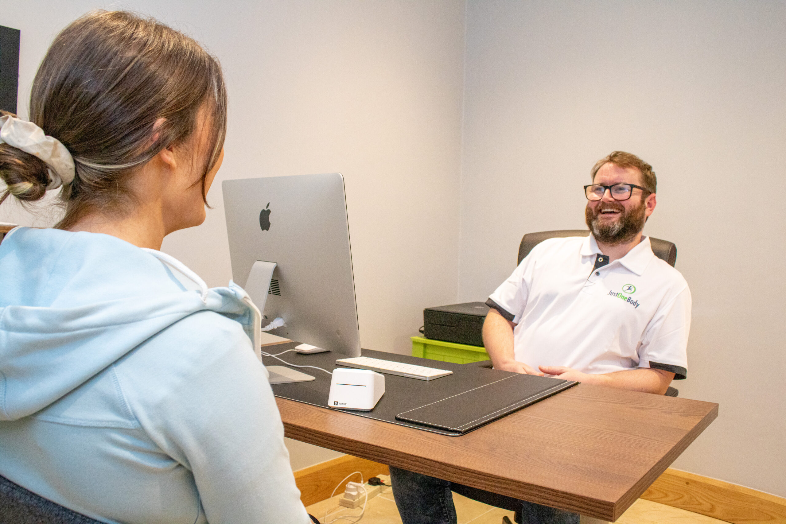 Kieran Lowe talking with a patient at the desk during a consultation at Just One Body