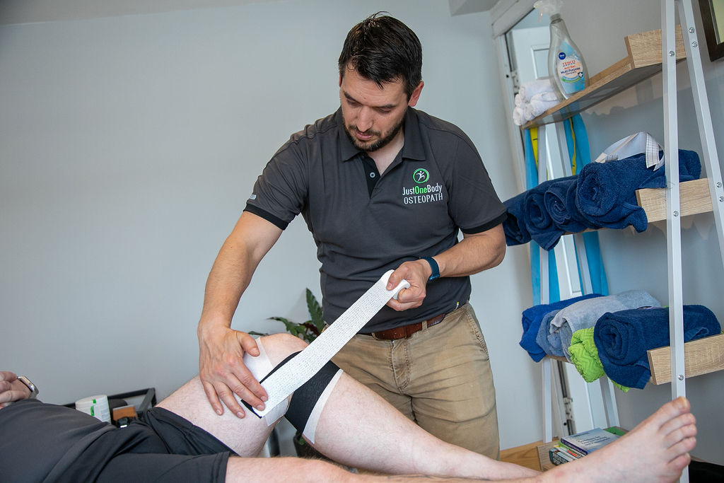 Kieran Lowe taping a patient's knee at Just One Body