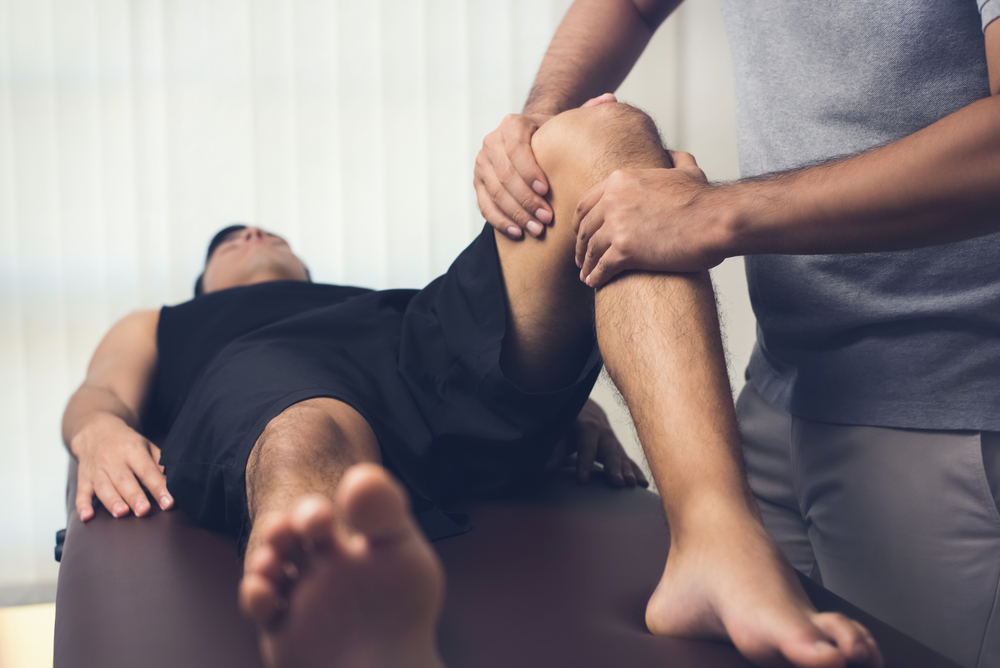 Therapist stretching a patient's hip and knee on a treatment table