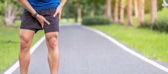Runner holding the front of his thigh on a tree-lined road