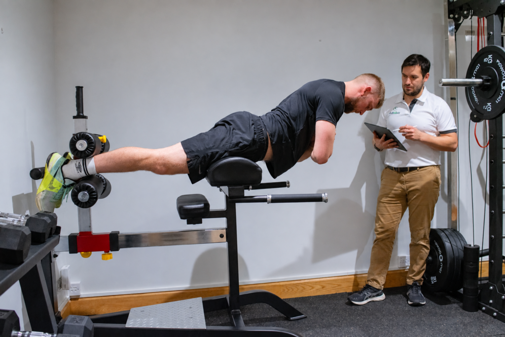 A patient doing a back extension exercise while a therapist watches at Just One Body, New Ross